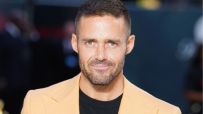Spencer Matthews, a man with short brown hair and a beard, wearing a light orange blazer and black shirt.