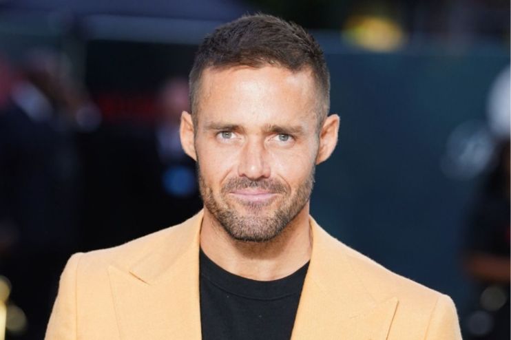 Spencer Matthews, a man with short brown hair and a beard, wearing a light orange blazer and black shirt.