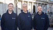 Three Tenora founders in navy hoodies smiling, standing outside a classical building with pillars