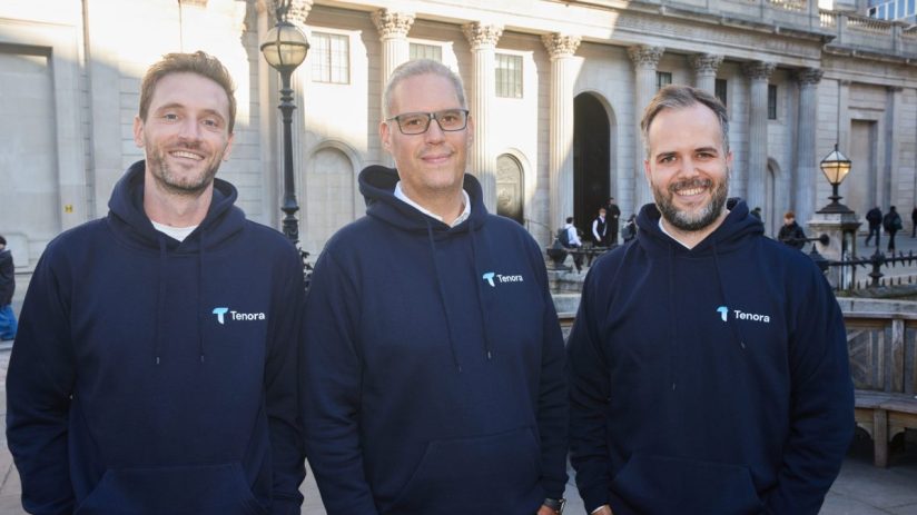 Three Tenora founders in navy hoodies smiling, standing outside a classical building with pillars