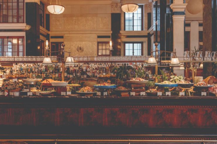 Lavish buffet spread at The Ned with diverse dishes, fresh salads, and a full bar in a grand, historic interior.