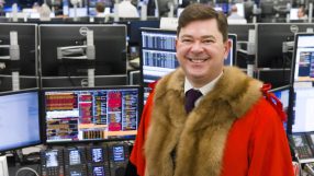 Tim Hailes smiling in official robes in a bustling trading office with multiple computer screens.