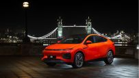 Bright orange XPeng G6 electric SUV parked on a paved street at night, with Londons Tower Bridge illuminated in the backgr...
