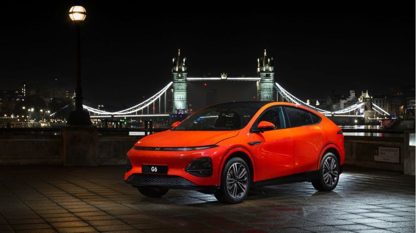Bright orange XPeng G6 electric SUV parked on a paved street at night, with Londons Tower Bridge illuminated in the backgr...