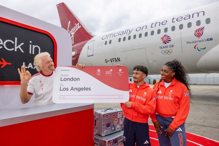 Richard Branson with Team GB athletes holding a London to Los Angeles boarding pass by a Virgin Atlantic plane.