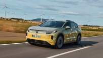 VW ID.4 Tiguan prototype in camouflage on a road with wind turbines in the background