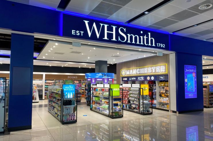 WHSmith store interior with prominent blue signage, display racks of books, travel items, and Manchester souvenirs.