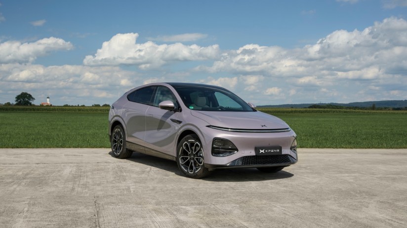XPENG New G6 electric SUV in light purple, parked on concrete with green fields and a blue sky in the background.