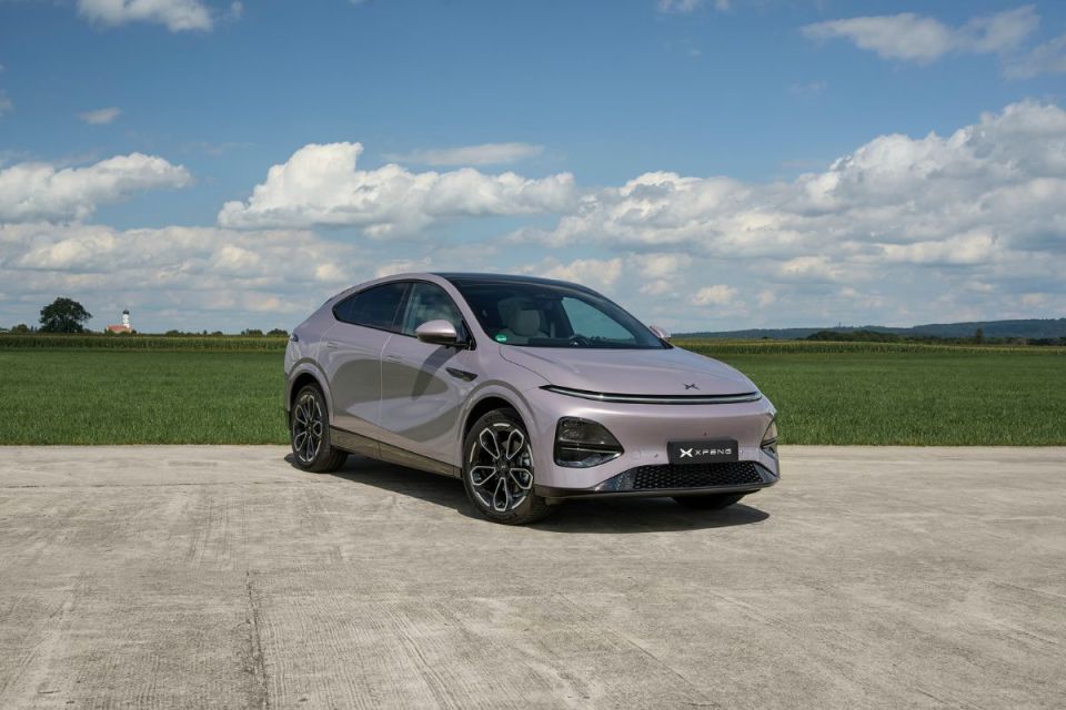 XPeng electric vehicle, a sleek gray SUV coupe, parked on concrete with a green field and blue sky background