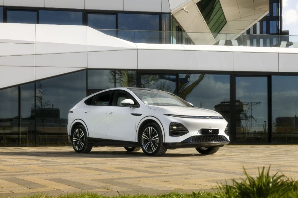 White XPeng G6 electric SUV parked on a paved area in front of a modern building with large windows.