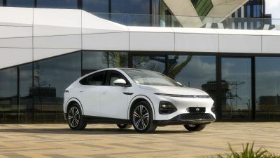 White XPeng G6 electric SUV parked on a paved lot in front of a modern building with large glass windows.