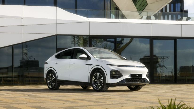 White XPeng G6 electric SUV parked on a paved lot in front of a modern building with large glass windows.