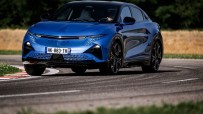 Blue Alpine electric car driving on a winding road with grass and fields in the background.