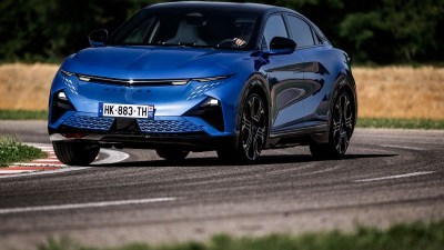 Blue Alpine electric car driving on a winding road with grass and fields in the background.