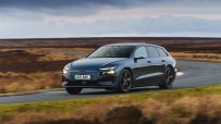 Dark blue Audi e-tron electric car driving on a winding road through a moorland landscape under cloudy skies