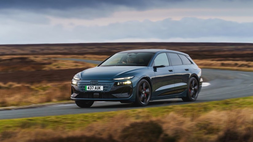 Dark blue Audi e-tron electric car driving on a winding road through a moorland landscape under cloudy skies