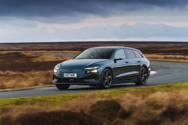 Dark blue Audi e-tron electric car driving on a winding road through a moorland landscape under cloudy skies