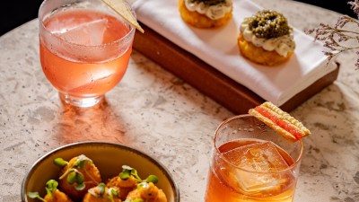 Cocktails and appetizers at Eve Bar by Martin Williams, including caviar blinis and arancini on a marble table.