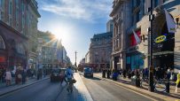 Bustling Oxford Street in London with shoppers, traffic, and iconic buildings under a sunny sky