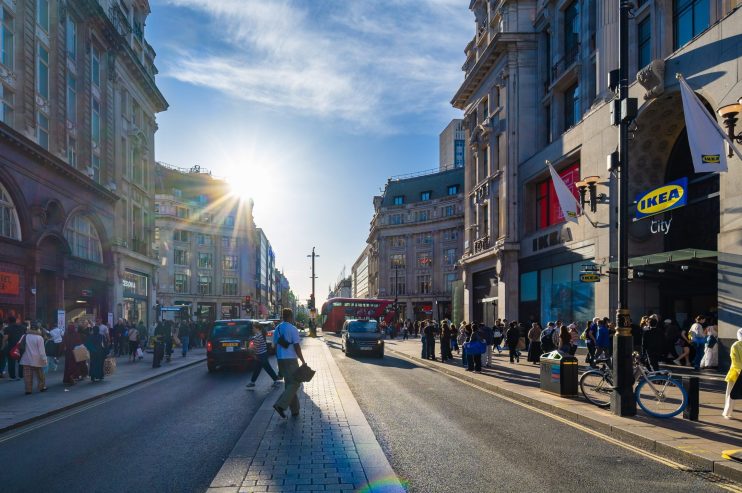 Bustling Oxford Street in London with shoppers, traffic, and iconic buildings under a sunny sky