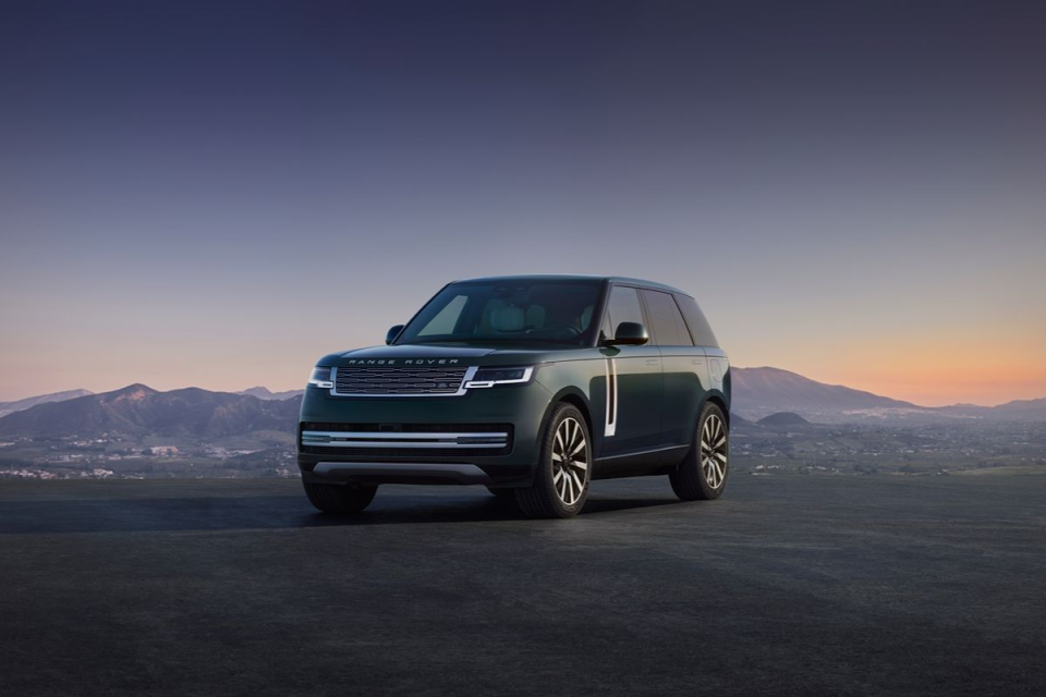 Dark green Range Rover parked on a paved surface with mountains and a sunset sky in the background.