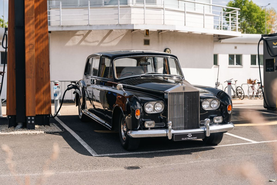 Black vintage Rolls-Royce car charging at an EV station with a modern white building in the background