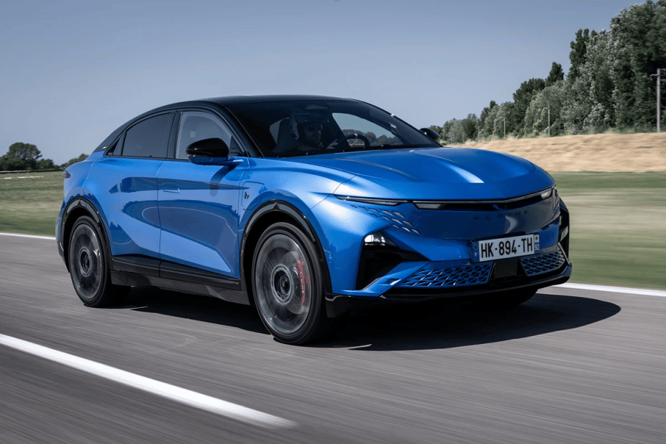 Dynamic blue Alpine A290 electric hatchback driving on a road, trees in background.