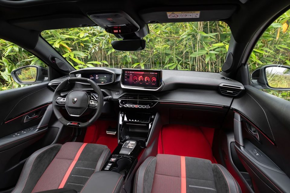 Modern car interior with black dashboard, red accents, digital displays, and red floor lighting.