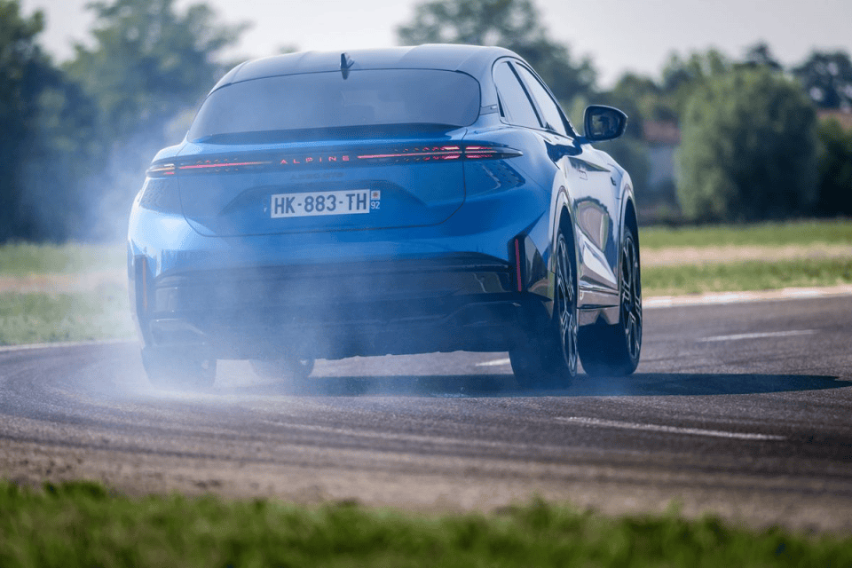 Blue Alpine A290 electric hot hatch drifting on a track, smoke from tires, rear view.