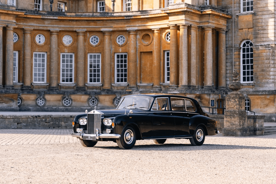 Black classic Rolls-Royce parked on a gravel drive in front of a grand, historic stone building.