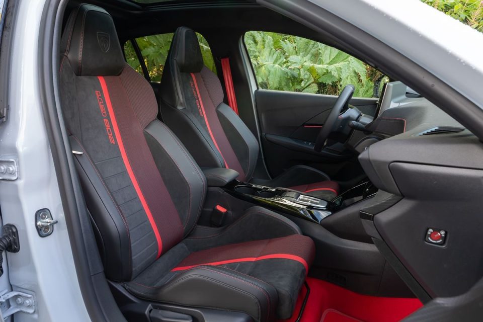 Interior of a modern car with black and red sport seats, red seatbelts, and a red floor mat.