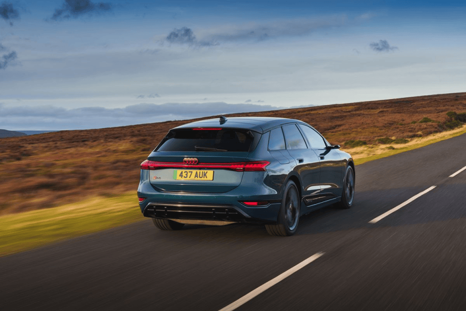 Dark green Audi e-tron GT driving on a winding country road with autumn-colored hillsides