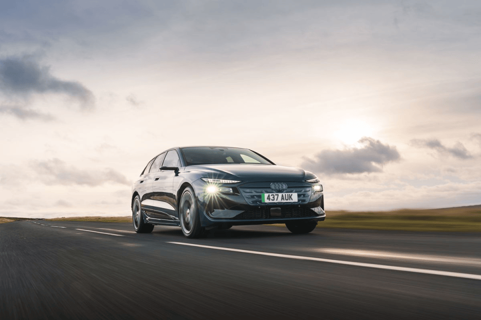 Dark grey Audi electric car driving fast on a highway at sunset, motion blur on road and wheels.
