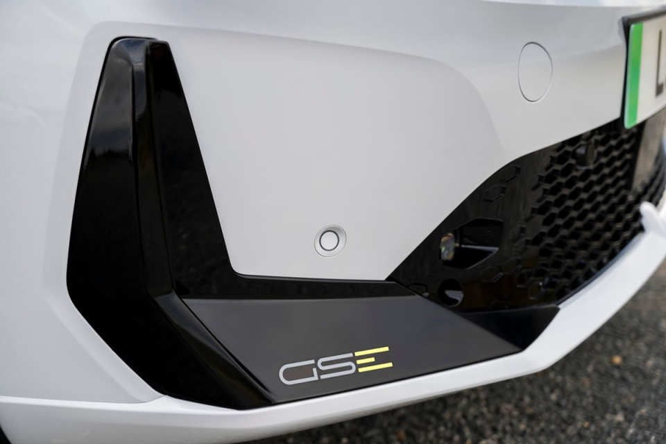Close-up of a white cars lower bumper with a black trim and GSe emblem, showing a parking sensor.