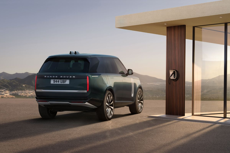 Dark green Range Rover parked at a modern electric vehicle charging station with mountains in the background.