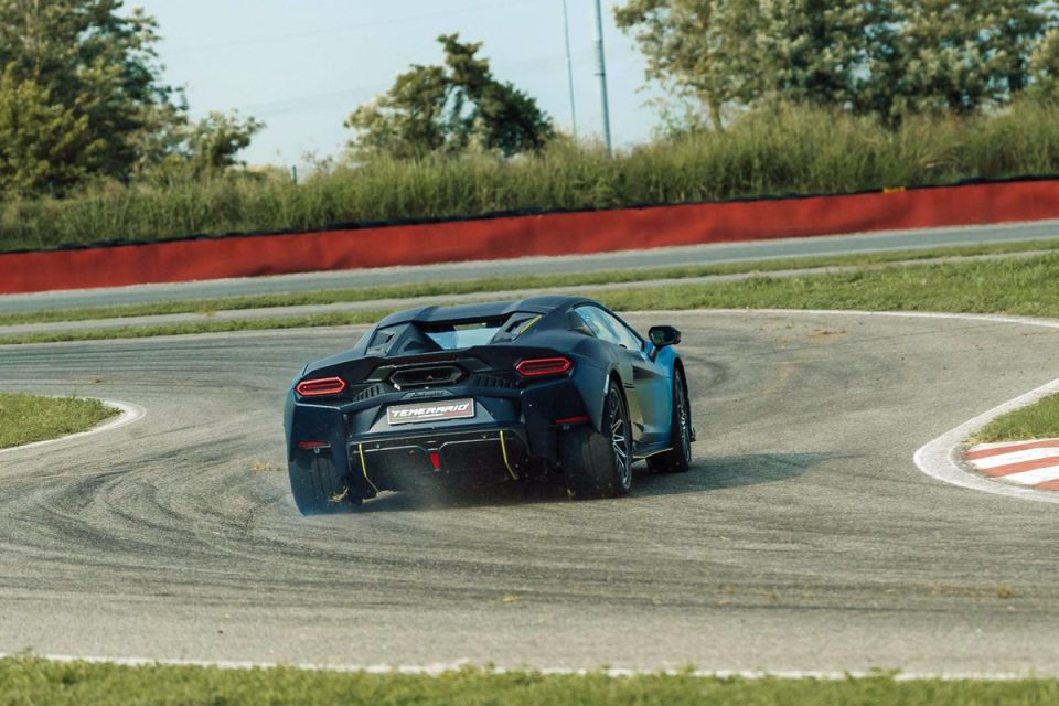 Dark blue sports car, Temerario on license plate, drifting on a racetrack with red and white curbs.