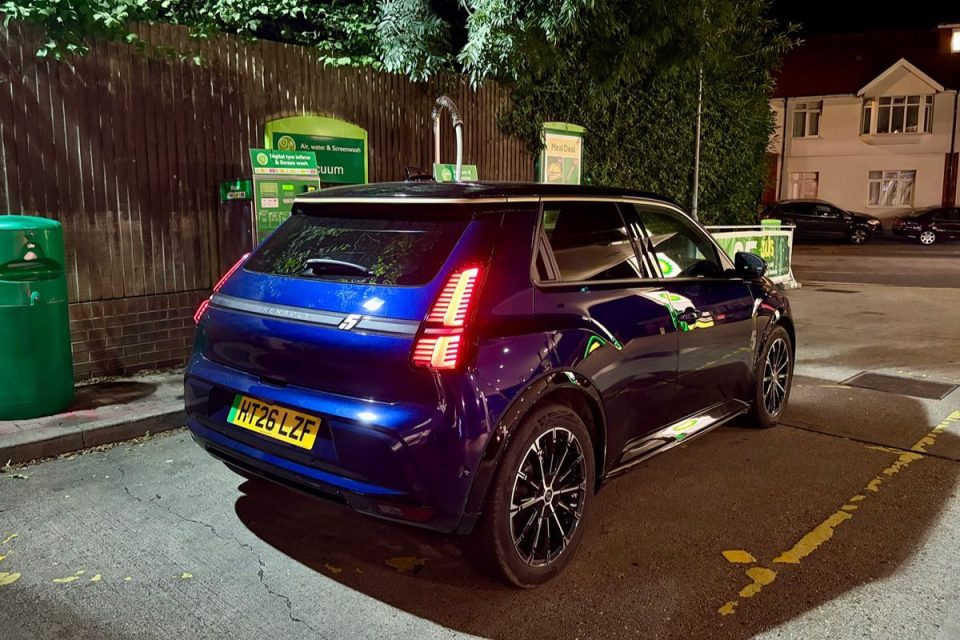 Blue electric car with illuminated taillights parked at a BP charging station at night.