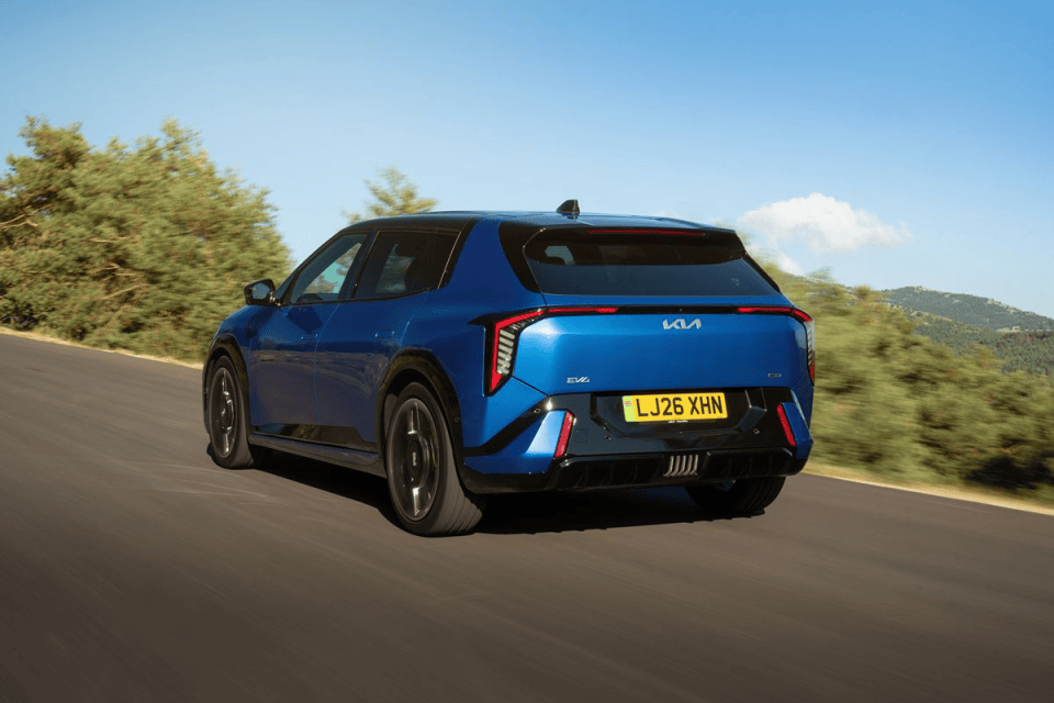 Blue Kia EV4 electric vehicle driving on a winding road with trees and hills in the background.