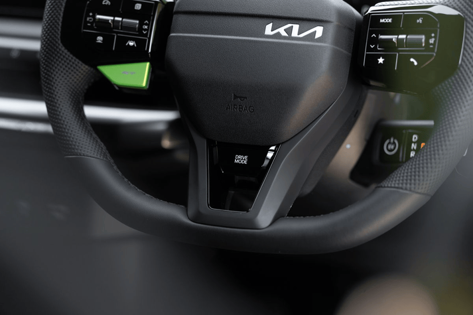 Close-up of a modern Kia steering wheel with controls, Drive Mode button, and green accent paddle shifter