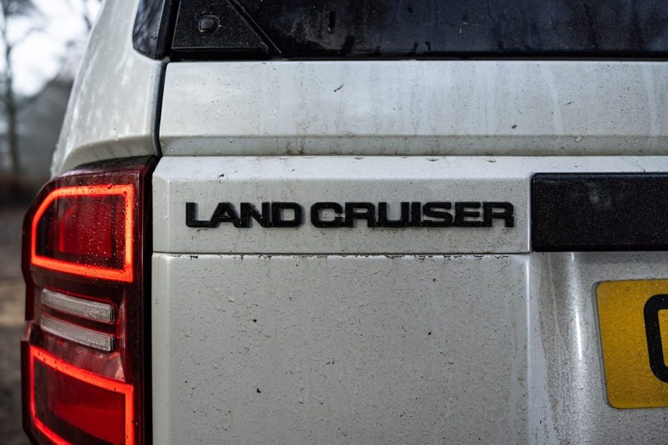 Close-up of a dirty, white Land Cruisers rear, showing the LAND CRUISER badge and part of a red taillight