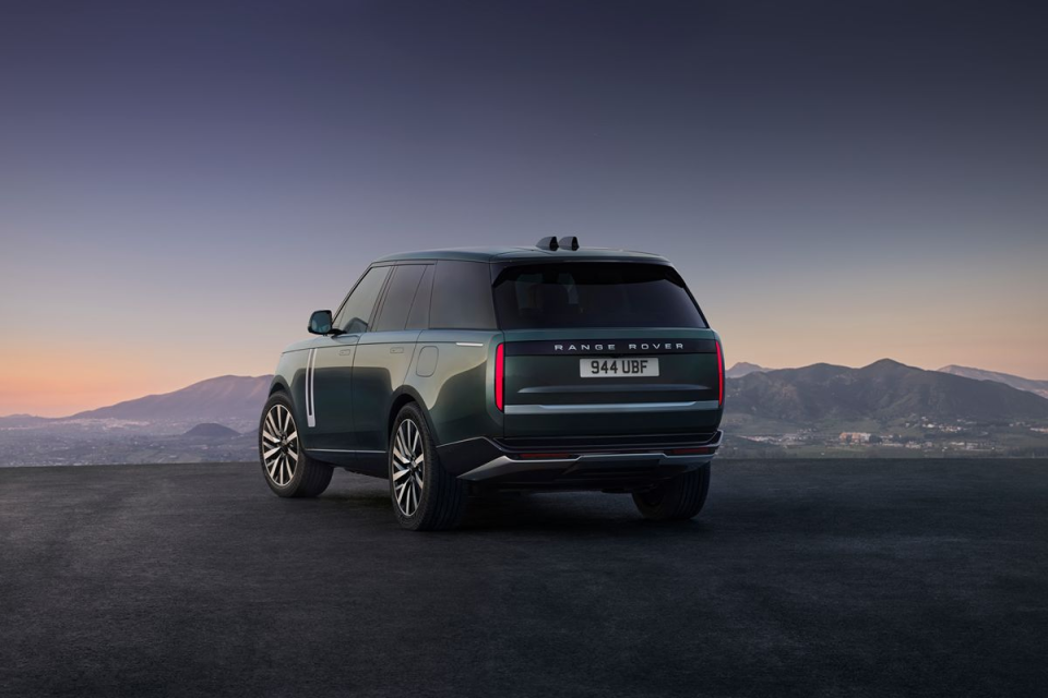 Dark green Range Rover SUV parked on an asphalt surface, overlooking a mountainous landscape at dusk.