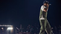 Jay-Z performing on stage at Tottenham Hotspur Stadium, wearing a cap, sunglasses, vest, and cargo pants.