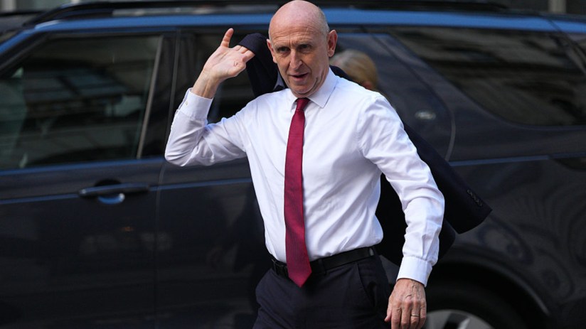 John Healey, wearing a white shirt and red tie, exits a vehicle, possibly discussing fiscal headroom.