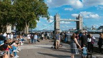 Crowd of tourists and locals walking along the Thames River with the iconic Tower Bridge in London, UK, on a sunny day.