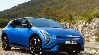 Blue Kia EV6 electric vehicle parked on a gravel road with a mountainous, treed background.