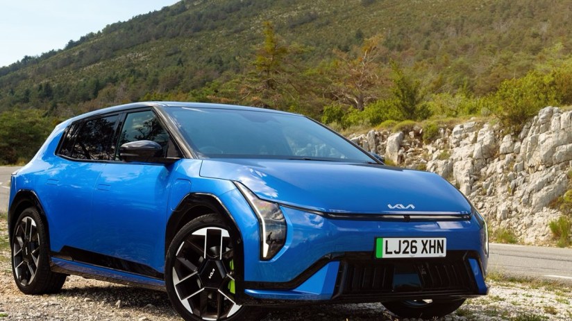 Blue Kia EV6 electric vehicle parked on a gravel road with a mountainous, treed background.