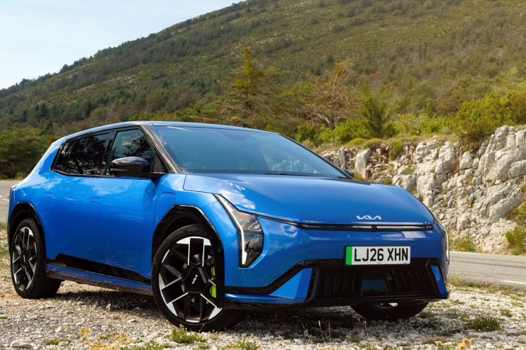 Blue Kia EV6 electric vehicle parked on a gravel road with a mountainous, treed background.