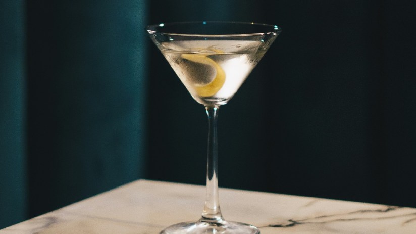 Classic martini cocktail with a lemon twist on a marble surface and dark background