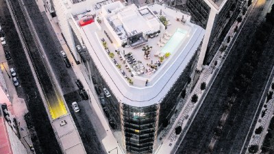 Aerial view of a modern building with a rooftop pool and lounge area, surrounded by city streets in Lisbon.