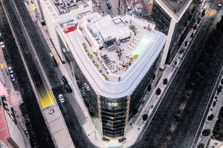 Aerial view of a modern building with a rooftop pool and lounge area, surrounded by city streets in Lisbon.